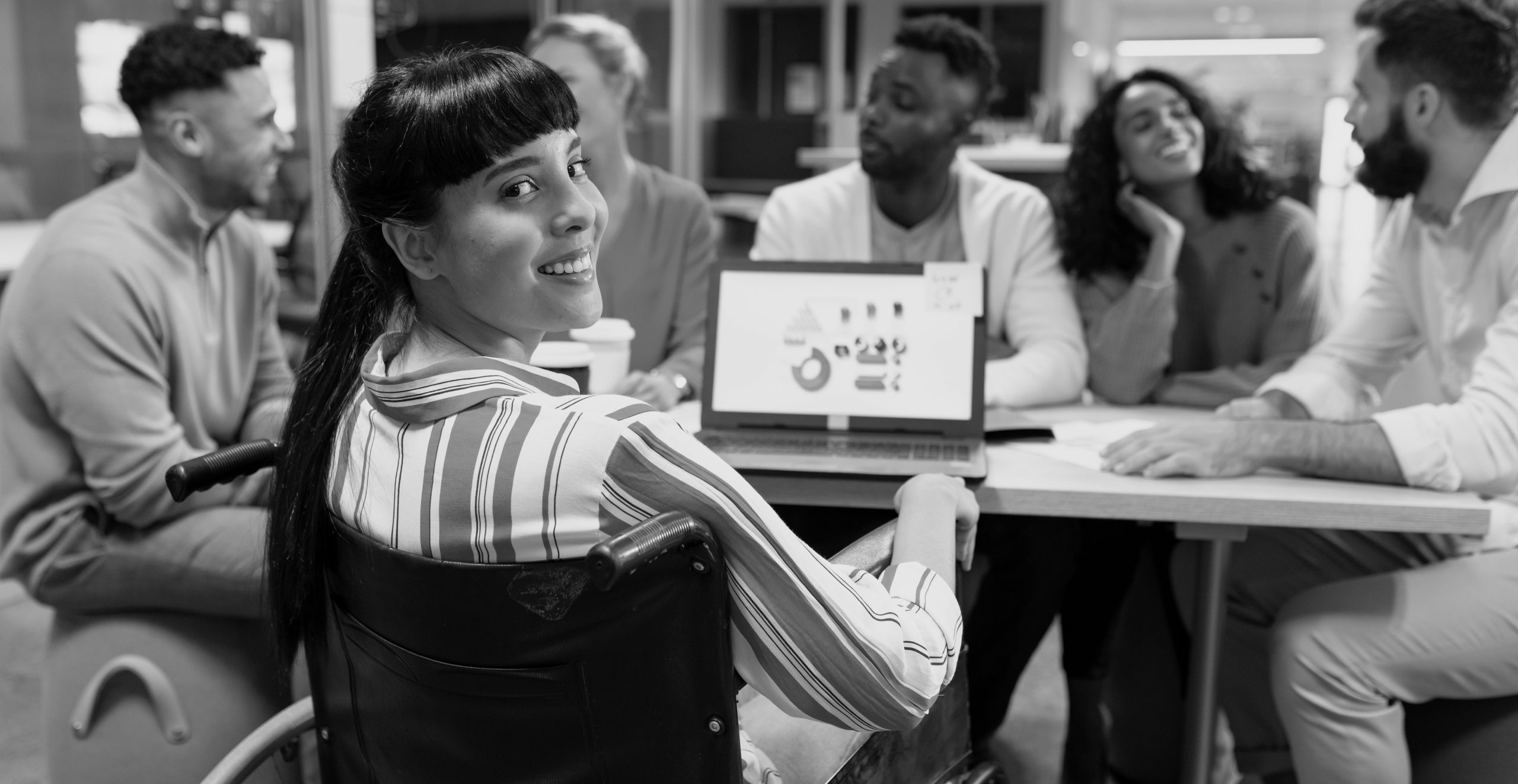 Smiling biracial disabled businesswoman looking over shoulder during meeting with colleagues