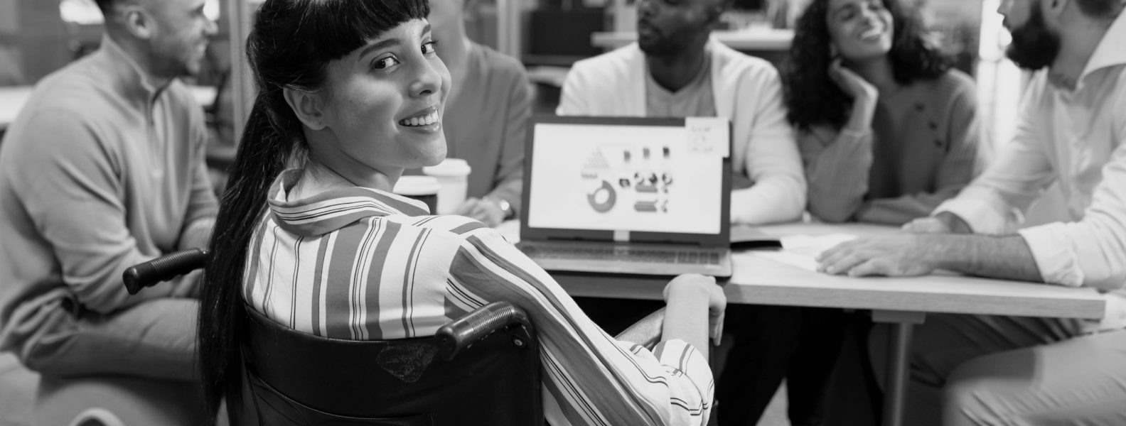 Smiling biracial disabled businesswoman looking over shoulder during meeting with colleagues